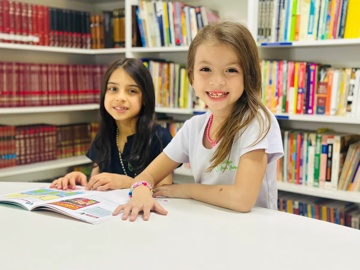 Duas alunas sorrindo durante uma atividade na biblioteca do colégio