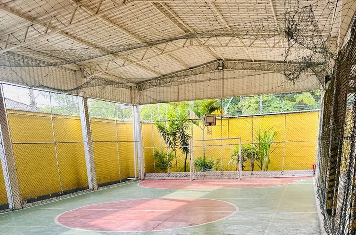 Quadra poliesportiva coberta do Colégio JJR, com traves, cesta de basquete e fechamento em tela