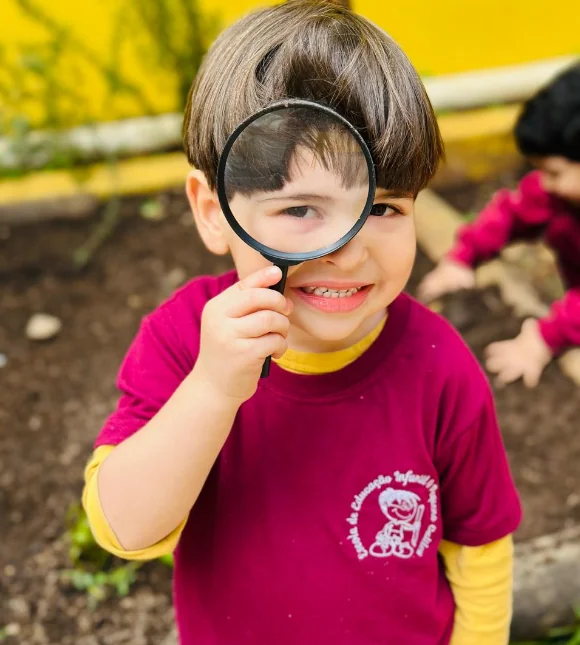 Criança da Educação Infantil observando o jardim com uma lupa